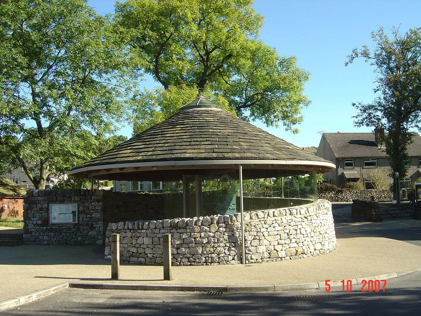 A stone and wood gazebo in the middle of a park.